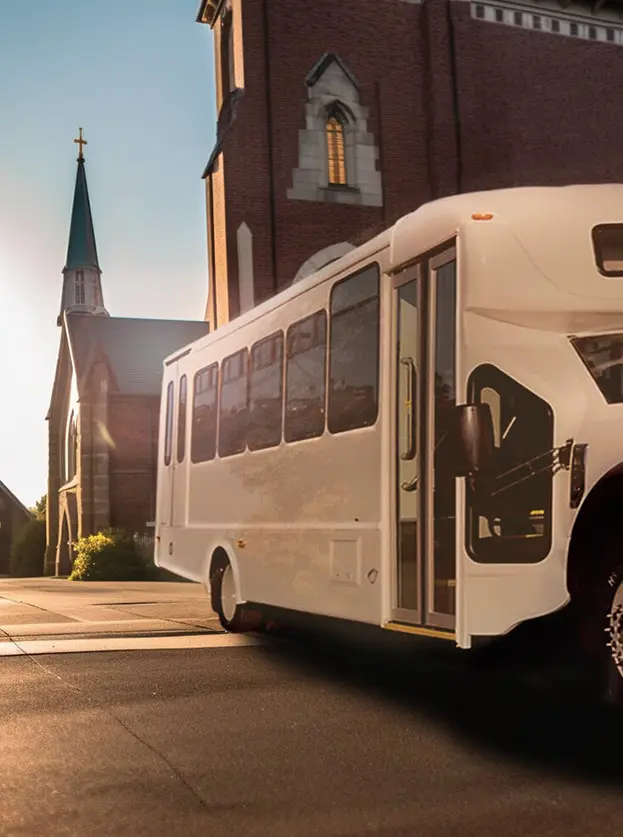white shuttle bus parked in front of a large brick church building